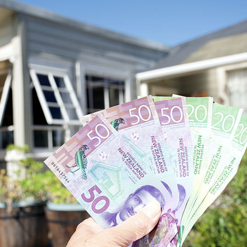 A hand holding New Zealand dollars after saving money on their inspection.